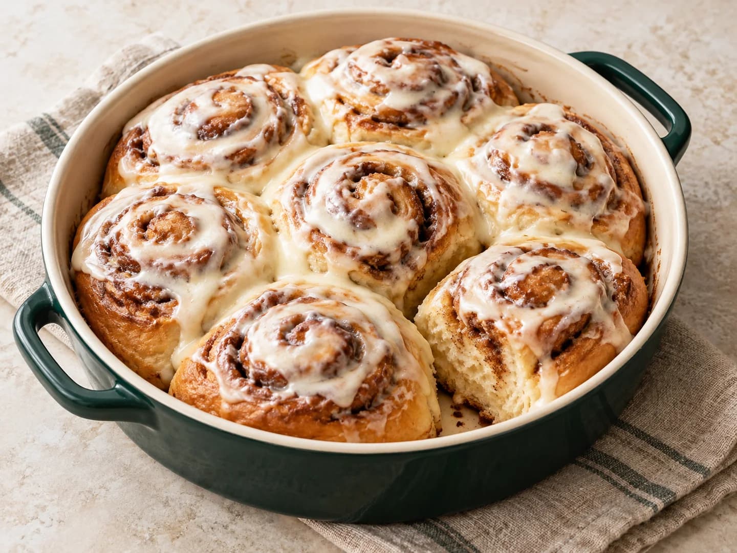 Homemade cinnamon rolls with brown-sugar filling and a simple cream frosting, styled with warm cream ceramic and deep-green tableware.