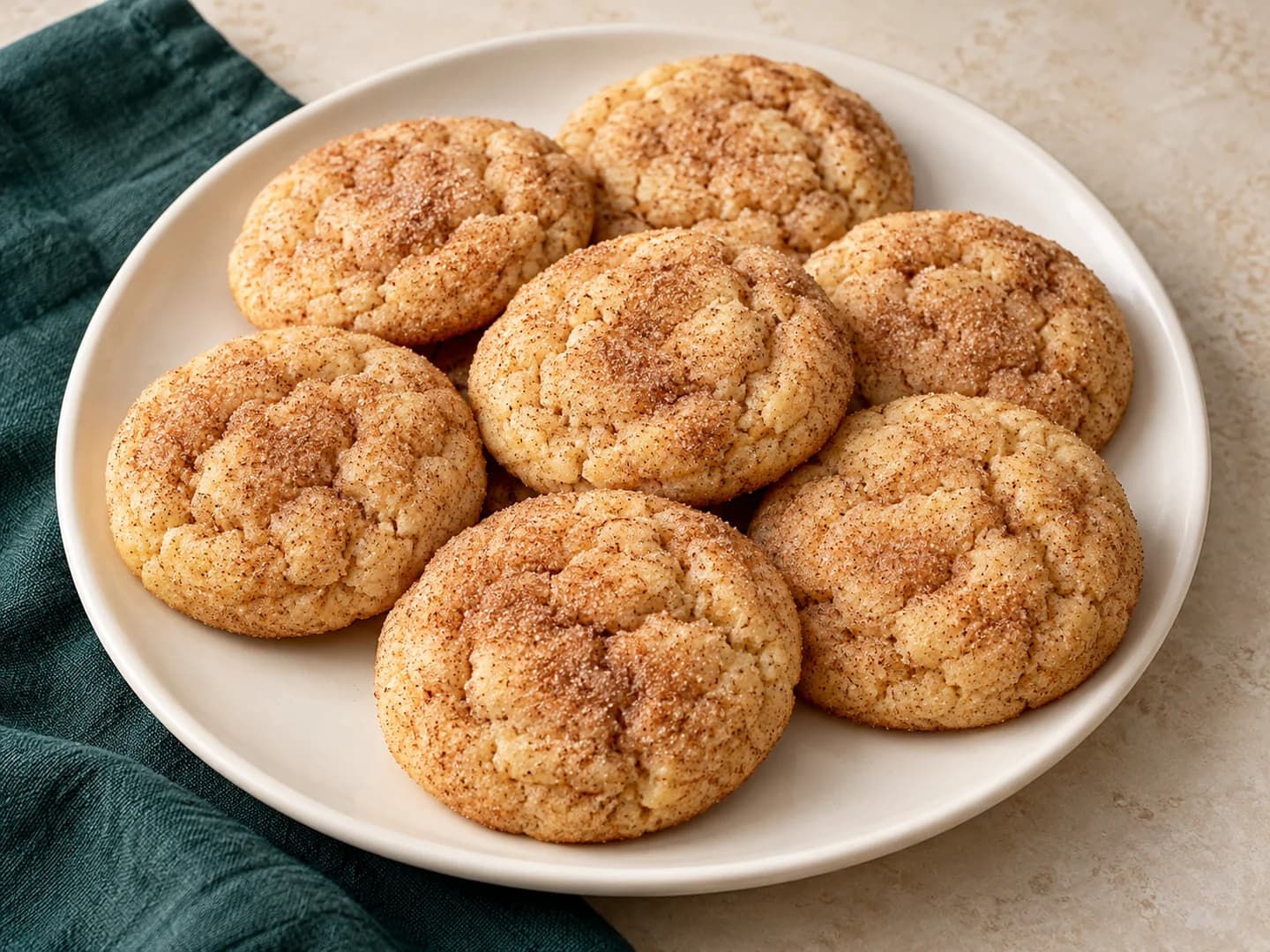 Classic snickerdoodles rolled in cinnamon sugar, styled with warm cream ceramic and deep-green tableware.
