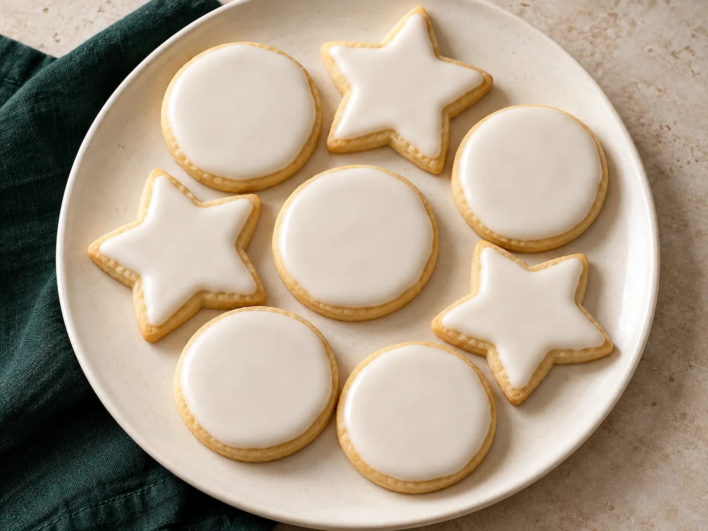 Chilled cutout sugar cookies with a simple powdered-sugar icing, styled with warm cream ceramic and deep-green tableware.