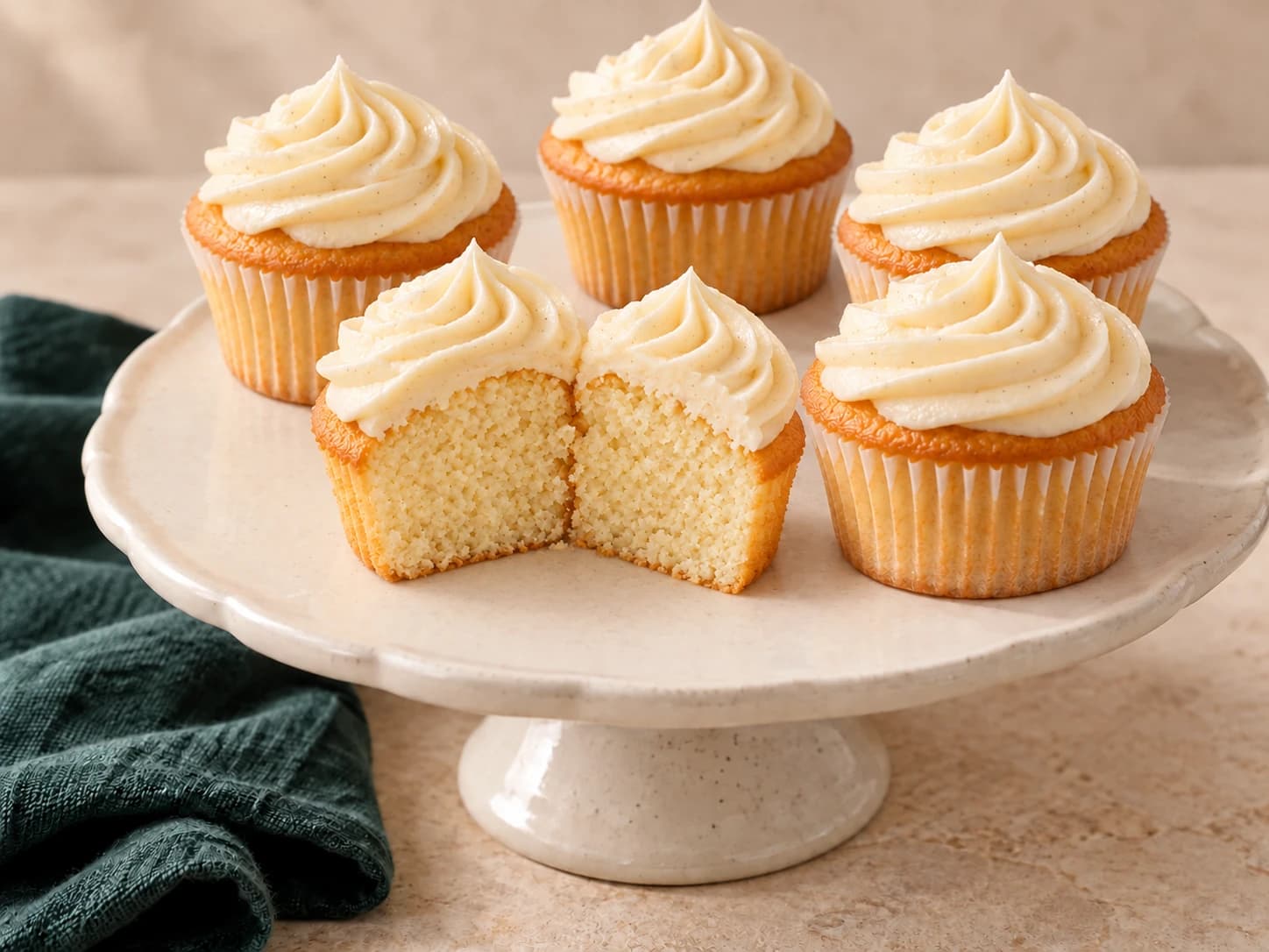 Vanilla cupcakes topped with swirls of ivory vanilla frosting, including one cut open to show the tender crumb.